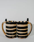 Two ceramic mugs with black and beige stripes on a light gray background