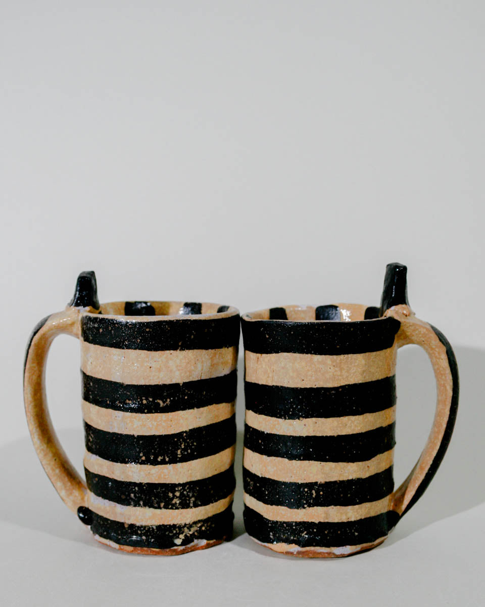 Two ceramic mugs with black and beige stripes on a light gray background